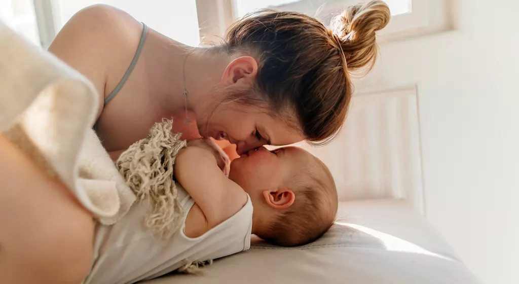 Mutter berührt liebevoll die Stirn ihres liegenden Babys
